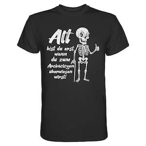Könnte beinhalten: Schwarzes T-Shirt mit einer weißen Skelettgrafik, die einen Daumen hoch zeigt und einen Stock hält. Das Shirt hat weißen Text, der lautet: "Alt bist du erst wenn du zum Archäologen überwiesen wirst!"