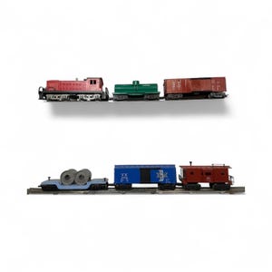 May include: A collection of vintage model train cars in red, green, and brown. The train cars are arranged on a track, with a red locomotive, a green tank car, and a brown boxcar on top. Below are a blue flatcar with metal coils, a blue boxcar, and a red caboose.