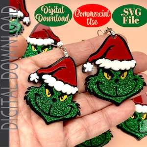 Puede incluir: Pendientes Grinch de purpurina verde con gorro de Papá Noel rojo y ribete blanco. Los pendientes tienen un contorno negro y ojos amarillos. La imagen también incluye el texto "Descarga digital", "Uso comercial" y ".SVG File".