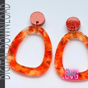 May include: A pair of orange resin earrings with a clear background and a glittery orange top. The earrings are shaped like an oval with a rounded top and bottom. The earrings are decorated with small orange leaves.