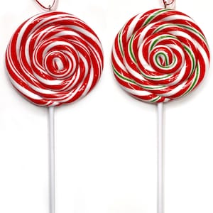 May include: Two red and white swirl lollipop ornaments, one with green stripes and one without. The lollipops are on white sticks.