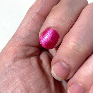 Puede incluir: Primer plano de una mano con una u&ntilde;a pintada de un rosa brillante con un acabado brillante. Las otras u&ntilde;as est&aacute;n desnudas y sin pintar.