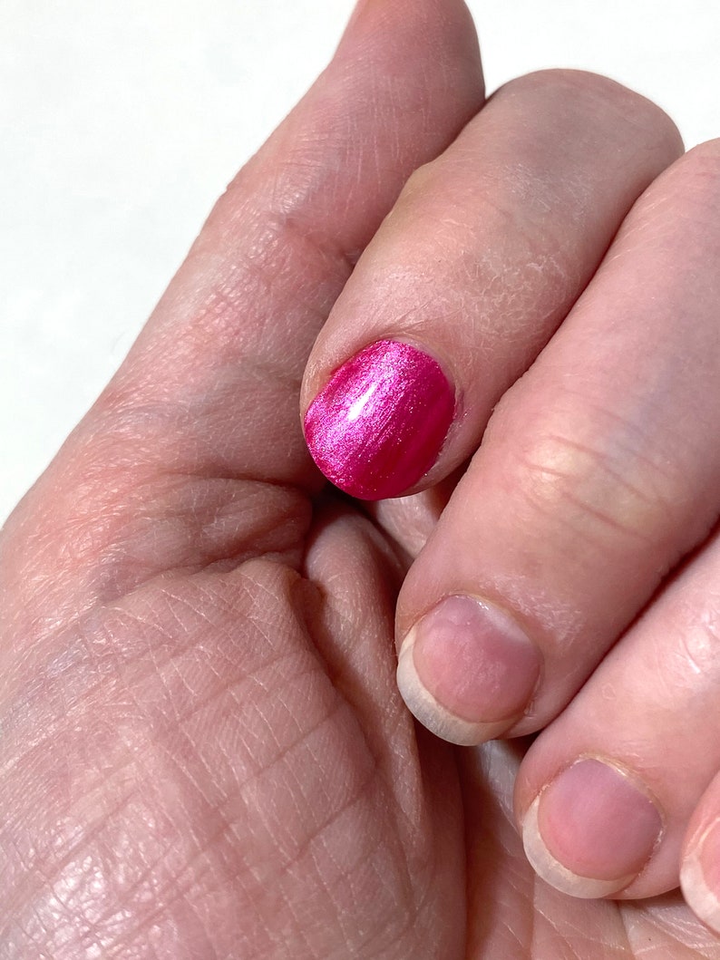 Puede incluir: Primer plano de una mano con una u&ntilde;a pintada de un rosa brillante con un acabado brillante. Las otras u&ntilde;as est&aacute;n desnudas y sin pintar.