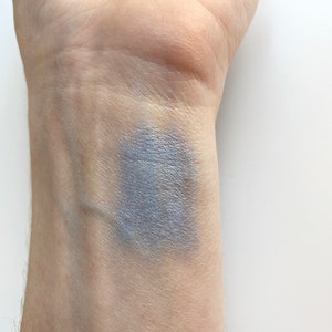 May include: A close-up of a person's wrist with a swatch of light blue eyeshadow applied to the skin.