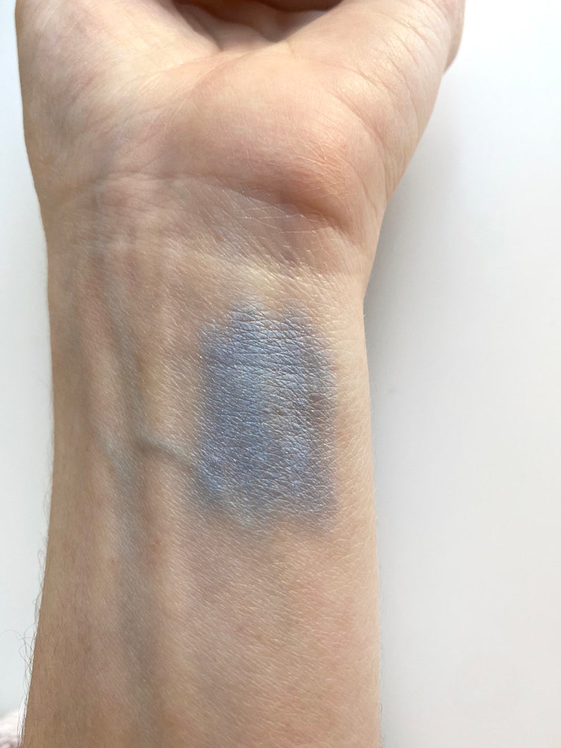 May include: A close-up of a person's wrist with a swatch of light blue eyeshadow applied to the skin.
