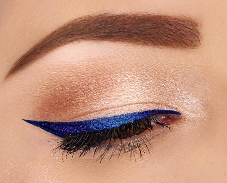 Peut inclure: Gros plan sur un &oelig;il avec un eye-liner bleu fonc&eacute; en forme d'aile. L'&oelig;il est entour&eacute; de fards &agrave; paupi&egrave;res neutres.