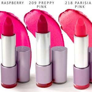 Op de afbeelding: Drie lippenstiftbuizen in verschillende roze tinten. De tinten zijn gelabeld "200 Raspberry", "209 Preppy Pink" en "218 Parisian Pink".