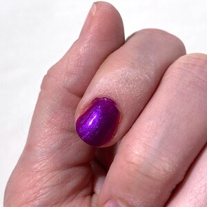 Puede incluir: Primer plano de un dedo con esmalte de u&ntilde;as morado con purpurina. El esmalte de u&ntilde;as es brillante y tiene un acabado met&aacute;lico.