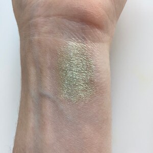 May include: A swatch of light green eyeshadow with a shimmery finish applied to a person's wrist.