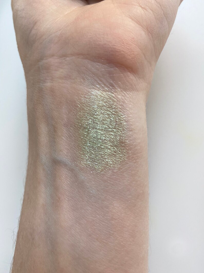 May include: A swatch of light green eyeshadow with a shimmery finish applied to a person's wrist.