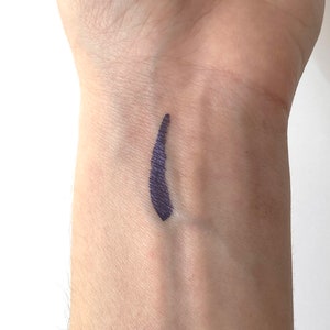 Peut inclure: Un gros plan sur le poignet d'une personne avec une ligne de couleur violet fonc&eacute; trac&eacute;e dessus. La ligne est lisse et uniforme, et semble avoir &eacute;t&eacute; r&eacute;alis&eacute;e avec un eye-liner liquide.