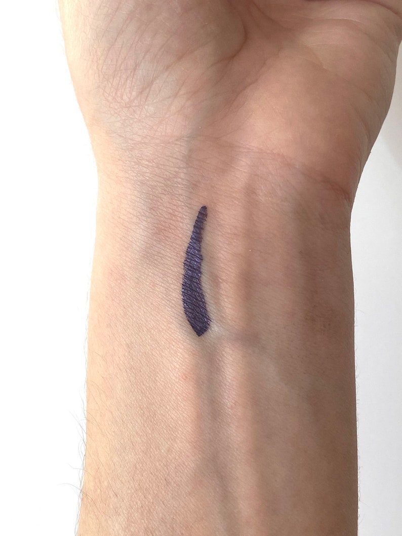 Peut inclure: Un gros plan sur le poignet d'une personne avec une ligne de couleur violet fonc&eacute; trac&eacute;e dessus. La ligne est lisse et uniforme, et semble avoir &eacute;t&eacute; r&eacute;alis&eacute;e avec un eye-liner liquide.