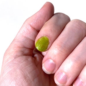 Puede incluir: Una mano con cuatro u&ntilde;as, una de las cuales est&aacute; pintada con un esmalte de u&ntilde;as verde brillante.