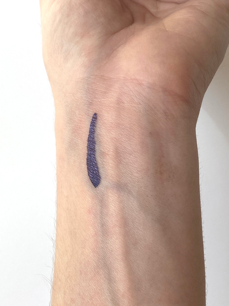 Peut inclure: Gros plan sur le poignet d'une personne avec une ligne de couleur violet fonc&eacute; trac&eacute;e dessus.