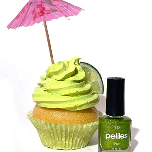 Puede incluir: Un cupcake verde con glaseado de lima y una rodaja de lima, coronado con una sombrilla de papel rosa. Una botella de esmalte de u&ntilde;as verde con purpurina est&aacute; al lado del cupcake. La etiqueta de la botella dice "pelites 580 Daze 0.25 fl oz."