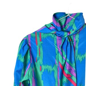 Peut inclure: Un chemisier à motif bleu, vert, rose et rouge avec un col montant et une cravate au cou.