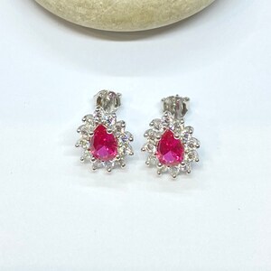 K&ouml;nnte beinhalten: Ein Paar silberne Ohrringe mit einem birnenf&ouml;rmigen roten Edelstein, der von kleineren wei&szlig;en Edelsteinen umgeben ist.