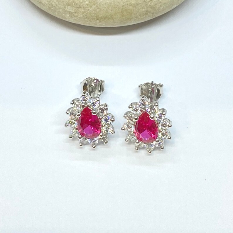 K&ouml;nnte beinhalten: Ein Paar silberne Ohrringe mit einem birnenf&ouml;rmigen roten Edelstein, der von kleineren wei&szlig;en Edelsteinen umgeben ist.