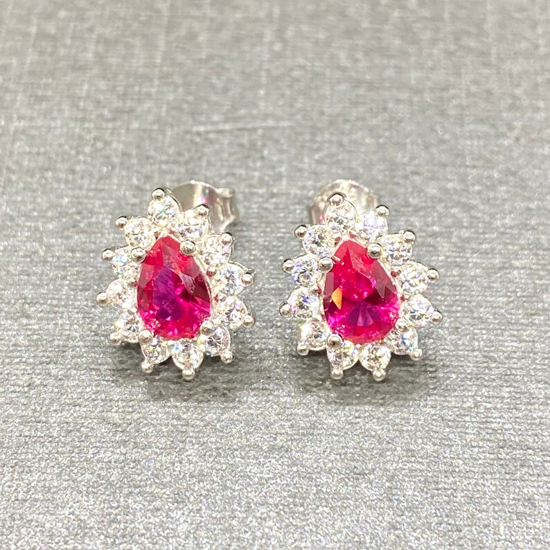 K&ouml;nnte beinhalten: Ein Paar silberne Ohrringe mit einem birnenf&ouml;rmigen rosa Stein, der von kleineren wei&szlig;en Steinen umgeben ist.