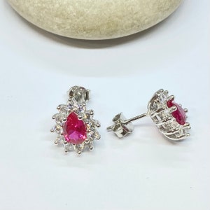 K&ouml;nnte beinhalten: Ein Paar silberne Ohrringe mit einem tropfenf&ouml;rmigen roten Edelstein, der von kleineren klaren Edelsteinen umgeben ist.