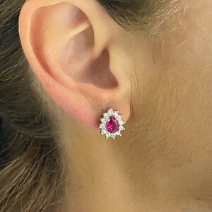 K&ouml;nnte beinhalten: Ein Paar silberne Ohrringe mit einem birnenf&ouml;rmigen Rubin, der von einem Heiligenschein aus kleineren wei&szlig;en Edelsteinen umgeben ist.