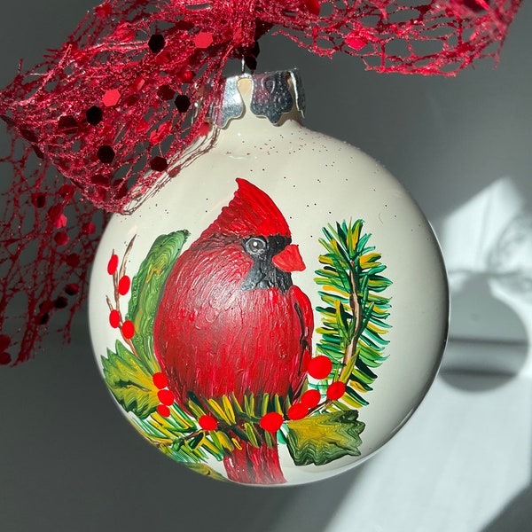 Hand Painted Glass Ornament approximately 2.75” diameter with a Cardinal sitting on pine branch and Red Sparkle Lace Bow.