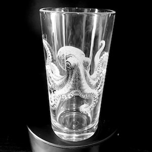 May include: A clear glass pint glass with an etched design of an octopus. The octopus is facing the right side of the glass and has its tentacles wrapped around the glass.
