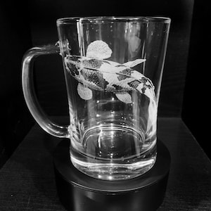 May include: A clear glass beer mug with a handle, featuring an etched design of a black and white fish.