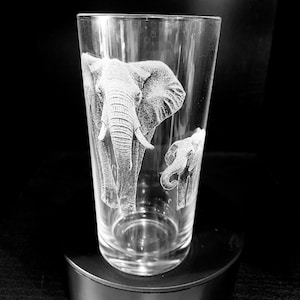 Op de afbeelding: Een helder glas met een gegraveerd ontwerp van twee olifanten. De grotere olifant loopt naar voren met zijn slurf omhoog. De kleinere olifant loopt achter de grotere olifant.