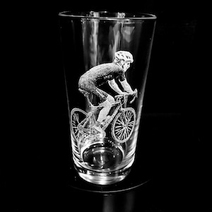 May include: A clear glass with an etched design of a cyclist riding a bicycle. The cyclist is wearing a helmet and is in mid-ride.