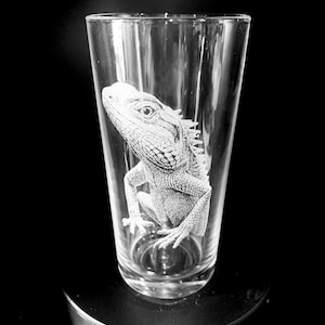 May include: A clear glass pint glass with an etched image of a white lizard.