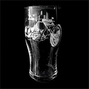 May include: A clear glass pint glass with a detailed etched design of a motorcycle. The motorcycle is depicted in a side profile, showcasing its wheels, engine, and frame. The glass has a curved shape and sits against a black background.