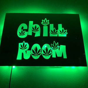 May include: A black sign with green LED lights behind it. The sign says "Chill Room" with marijuana leaf cutouts in the letters.