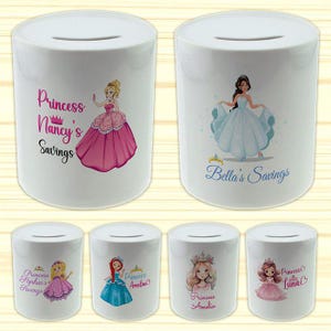 May include: White ceramic money banks with princess designs. Each bank features a princess illustration and the text "Princess Nancy's Savings", "Bella's Savings", "Princess Sophia's Savings", "Princess Amelia", and "Princess Luna's Savings".
