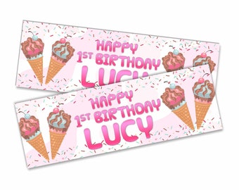 May include: Two pink and white banners with the text "Happy 1st Birthday Lucy" in pink letters. The banners are decorated with ice cream cones and sprinkles.