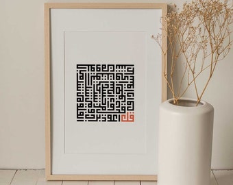 May include: A framed print with a black and white Arabic calligraphy design. The design is in a square shape and features a red word in the center. The print is hanging on a white wall.