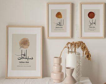 May include: Three framed prints with beige backgrounds and brown leaf illustrations. Each print features Arabic calligraphy and a translation in English. The prints are displayed on a white table with a white vase and two pink vases.