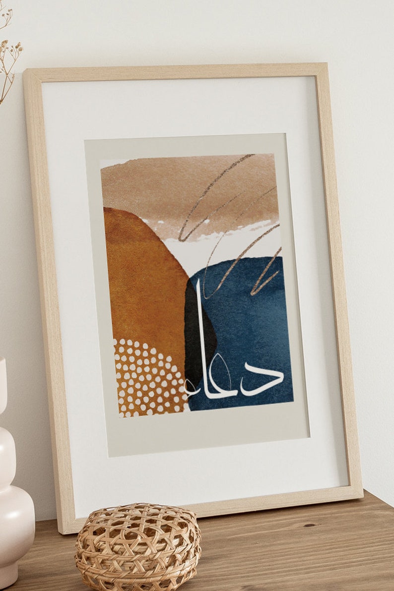 May include: A framed abstract art print with a beige background, featuring a blue, brown, and black geometric design with white polka dots and the Arabic word "حلم" (meaning "dream") in white.