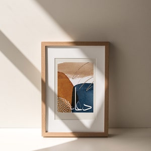 May include: A framed abstract art print with a brown, orange, blue, and white colour scheme. The print features abstract shapes and lines, and the text "حال" is written in white.