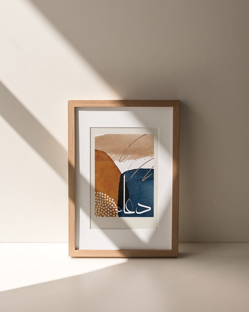 May include: A framed abstract art print with a brown, orange, blue, and white colour scheme. The print features abstract shapes and lines, and the text "حال" is written in white.