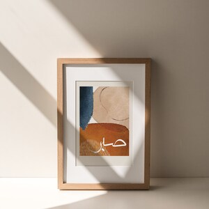 May include: A framed abstract art print with a beige, blue, and orange colour scheme. The Arabic word "حب" is written in white in the centre of the print.