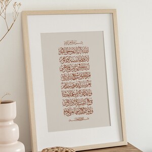 Op de afbeelding: Een ingelijst afdruk met een beige achtergrond en bruine Arabische kalligrafie. De tekst luidt "بسم الله الرحمن الرحيم" en gaat verder met een reeks verzen in het Arabisch.