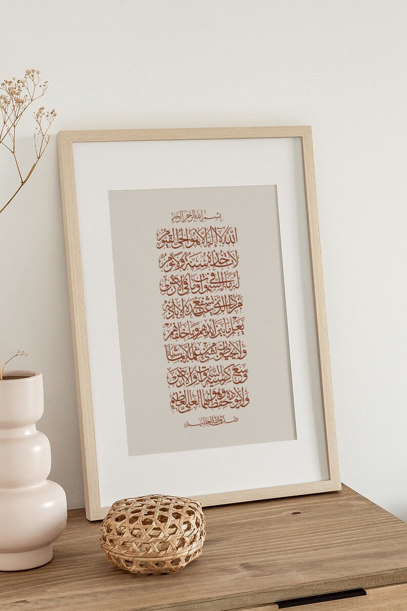 Op de afbeelding: Een ingelijst afdruk met een beige achtergrond en bruine Arabische kalligrafie. De tekst luidt "بسم الله الرحمن الرحيم" en gaat verder met een reeks verzen in het Arabisch.