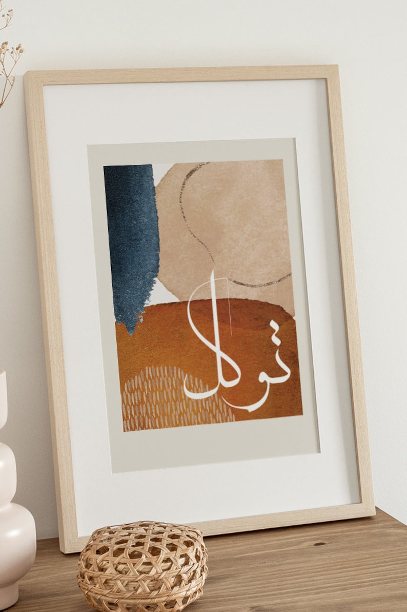 May include: A framed print with an abstract design featuring a blue, brown, and beige colour scheme. The print includes Arabic calligraphy in white.