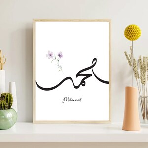Puede incluir: Una impresi&oacute;n de arte imprimible blanca con un dise&ntilde;o de caligraf&iacute;a negra de la palabra &aacute;rabe para "Muhammad" con un peque&ntilde;o dise&ntilde;o de flor de acuarela en la esquina superior izquierda.