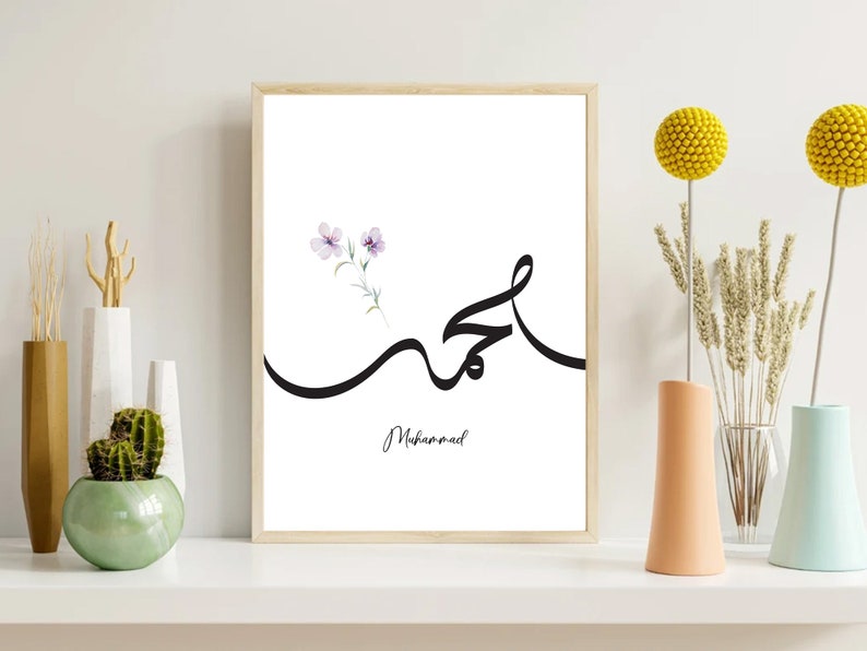 Puede incluir: Una impresi&oacute;n de arte imprimible blanca con un dise&ntilde;o de caligraf&iacute;a negra de la palabra &aacute;rabe para "Muhammad" con un peque&ntilde;o dise&ntilde;o de flor de acuarela en la esquina superior izquierda.