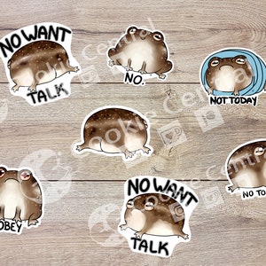 May include: A collection of seven die-cut stickers featuring cartoon frogs in various poses. Each frog is brown with white spots and has a different expression. Text on the stickers includes "NO WANT TALK", "NO.", "NOT TODAY", "OBEY", and "NO TOUCH".