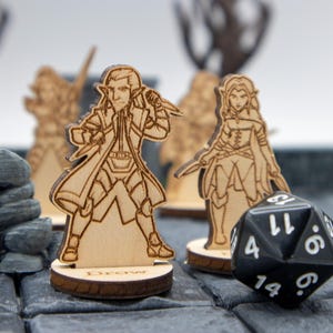 May include: Four wooden miniature figures of fantasy characters, including a drow, a human, and two elves, stand on bases. A black 20-sided die with white numbers is in the foreground.