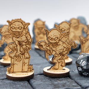 May include: A set of six wooden goblin miniatures, each with a unique pose and expression. The goblins are painted in shades of brown and have a detailed design. A black and white dice is also included in the image.