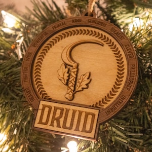 May include: A wooden ornament with a circular design featuring a stylized sickle and leaves. The ornament is inscribed with the words "DRUID" and a list of positive attributes, including "wise", "powerful", "healer", "fighter", "philosopher", "intelligent", "clever", "idealist", "generous", "king", "primal", and "know".